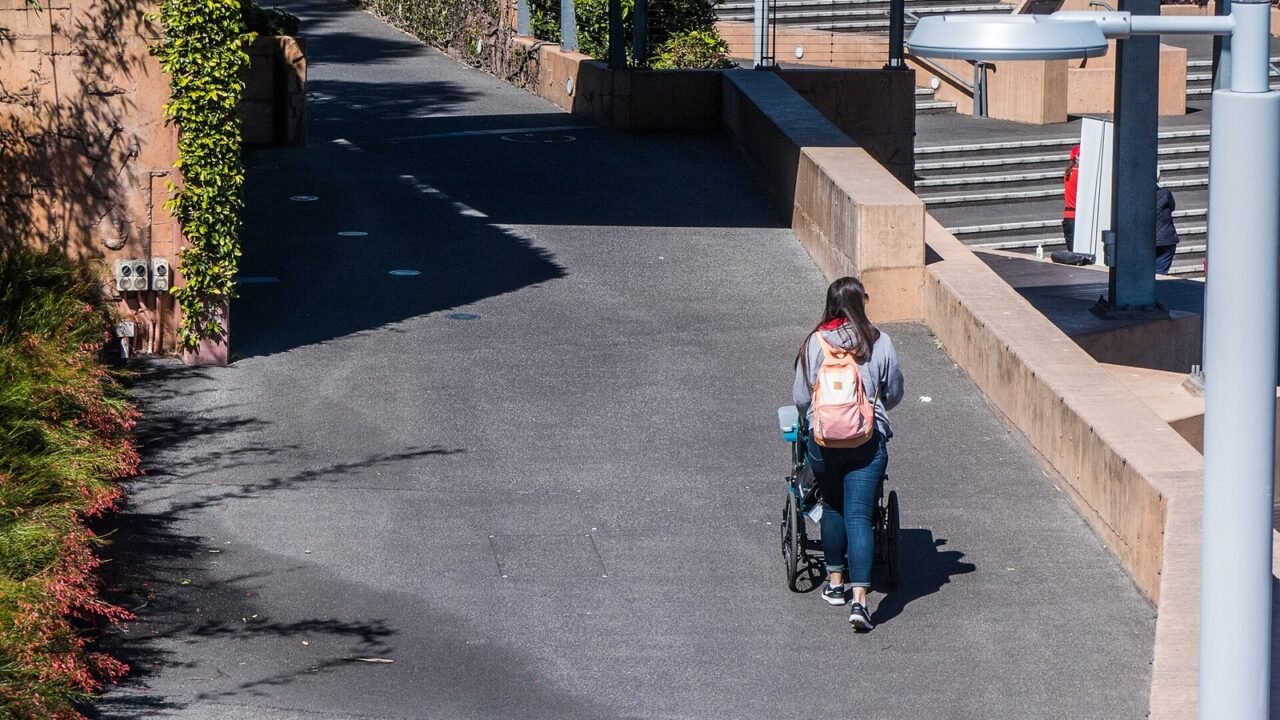 Person schiebt einen Rollstuhl einen Weg entlang (Symbolbild)