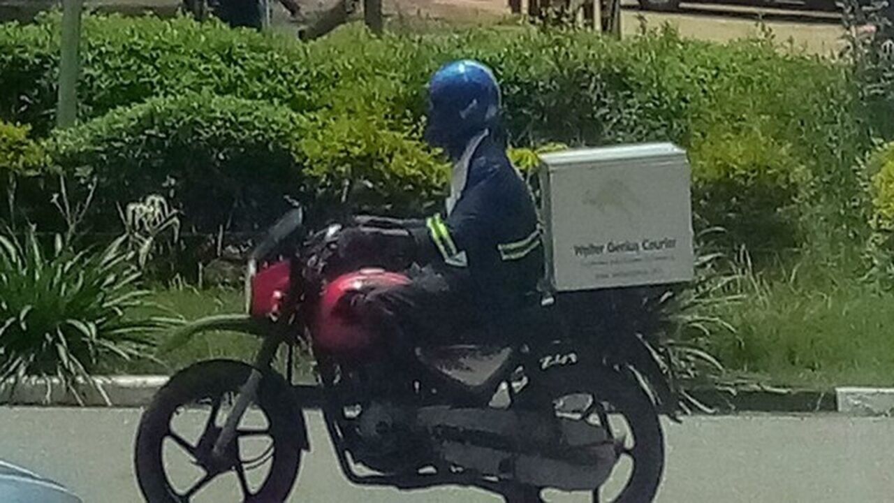 Kurierfahrer mit Helm und Lieferbox auf einem Motorrad (Symbolbild)