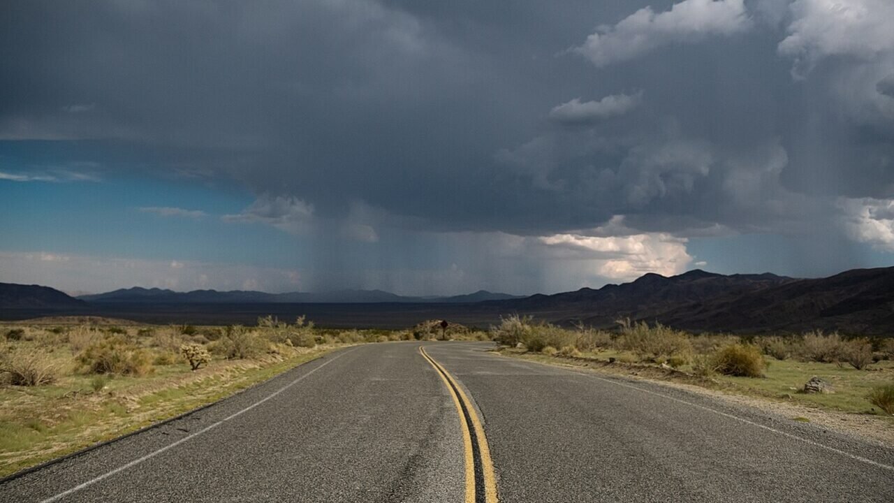 Dunkle Gewitterwolken über einer Wüstenlandschaft mit Straße (Symbolbild)