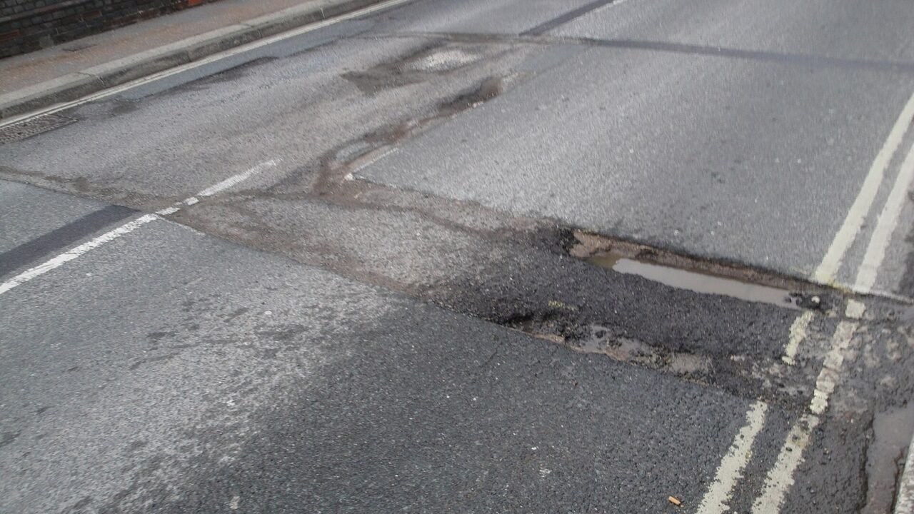 Beschädigte Straße mit Schlagloch und Pfütze (Symbolbild)