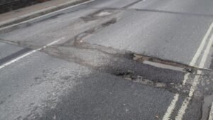 Beschädigte Straße mit Schlagloch und Pfütze (Symbolbild)