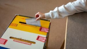 Stimmzettel wird in eine versiegelte Wahlurne geworfen (Symbolbild)